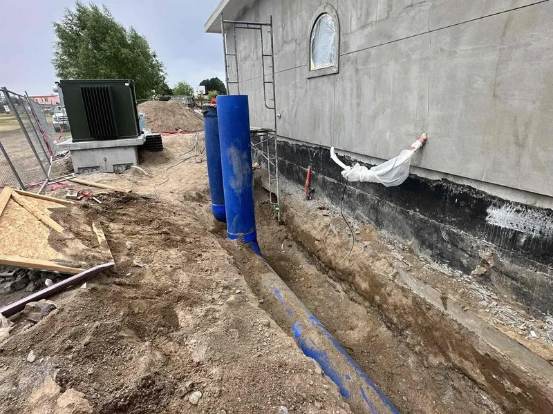 An open trench beside a building with underground duct being laid