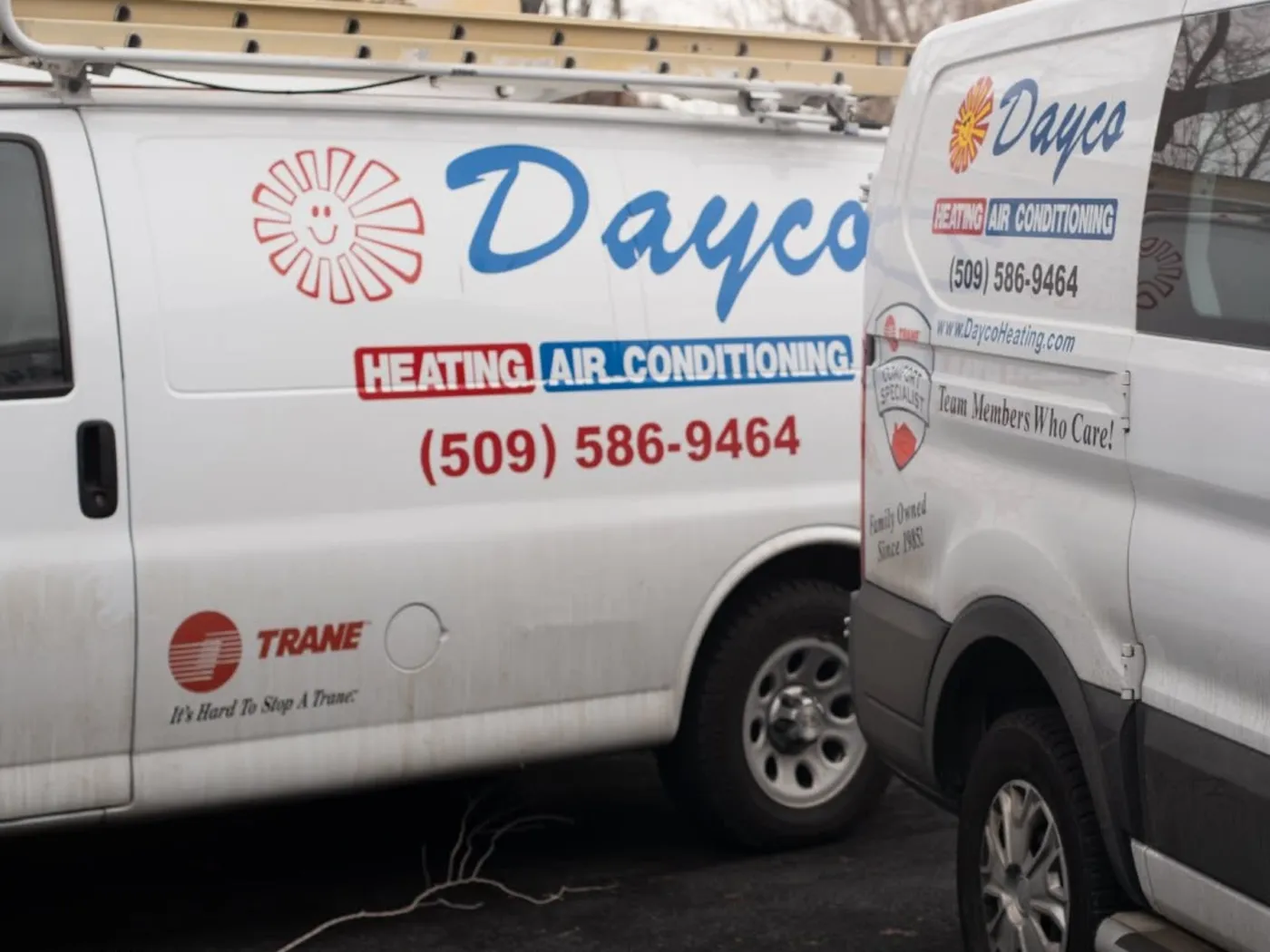 Two white Dayco service vans with the sun logo and the phone number (509) 586-9464 on the side