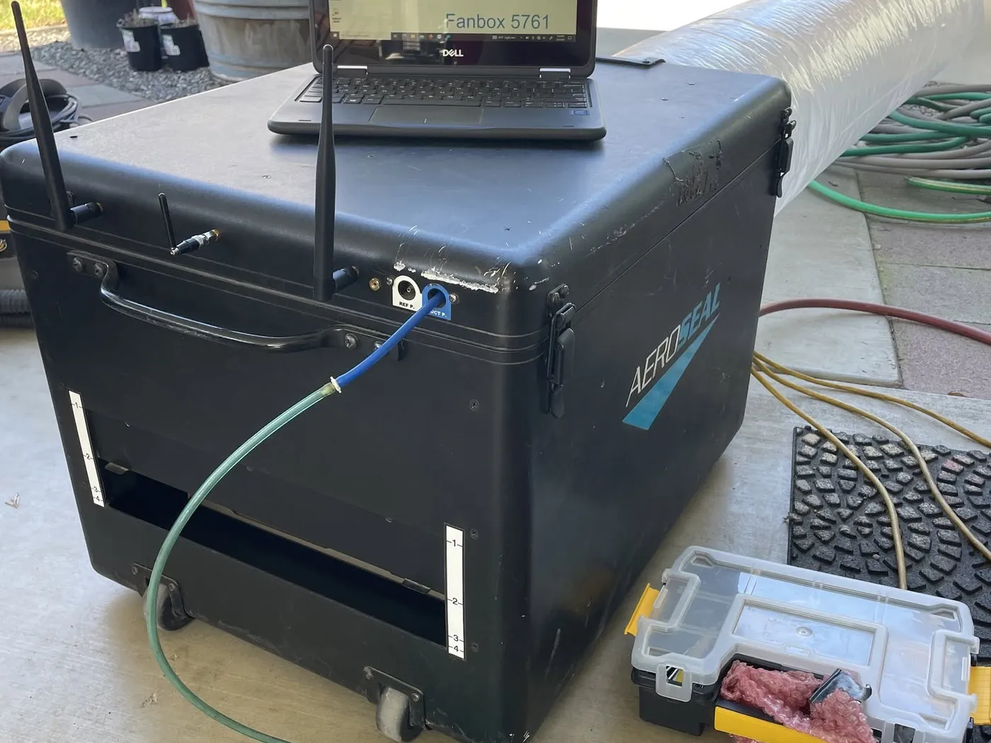 An Aeroseal sealing machine with a laptop on top, hosed into a home’s ductwork