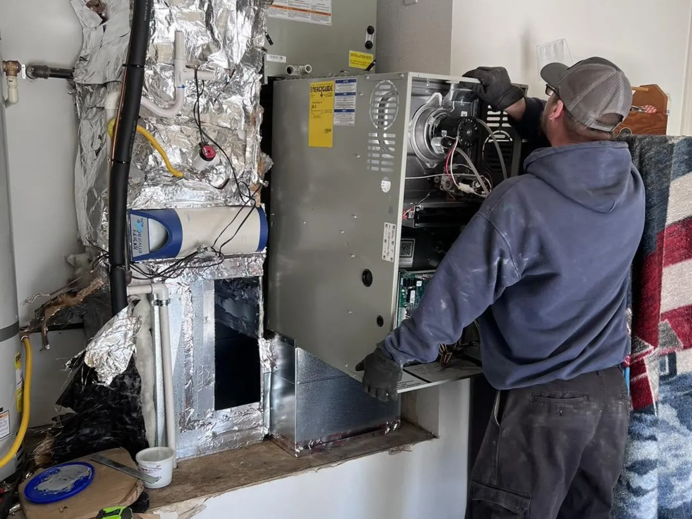 A Dayco installer fitting a new furnace into its ductwork in a utility closet