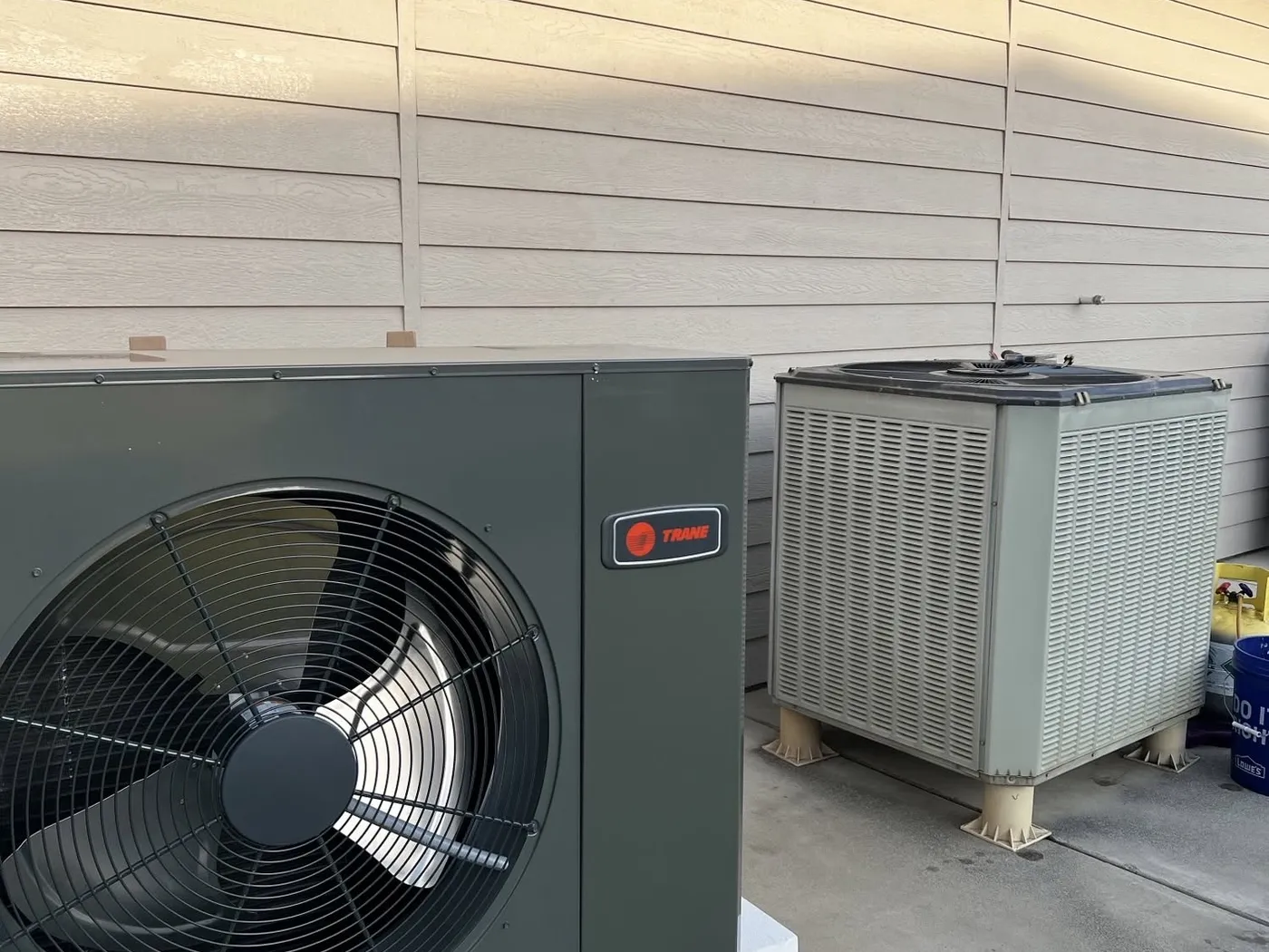 Two new Trane outdoor heat pump units installed side by side against a house