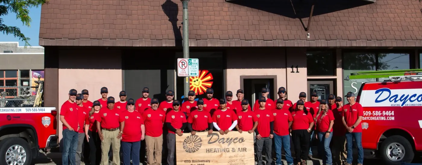 The Dayco crew in red company shirts in front of the Dayco shop at 11 N Auburn in Kennewick, holding a 40th anniversary sign, with Dayco trucks on either side